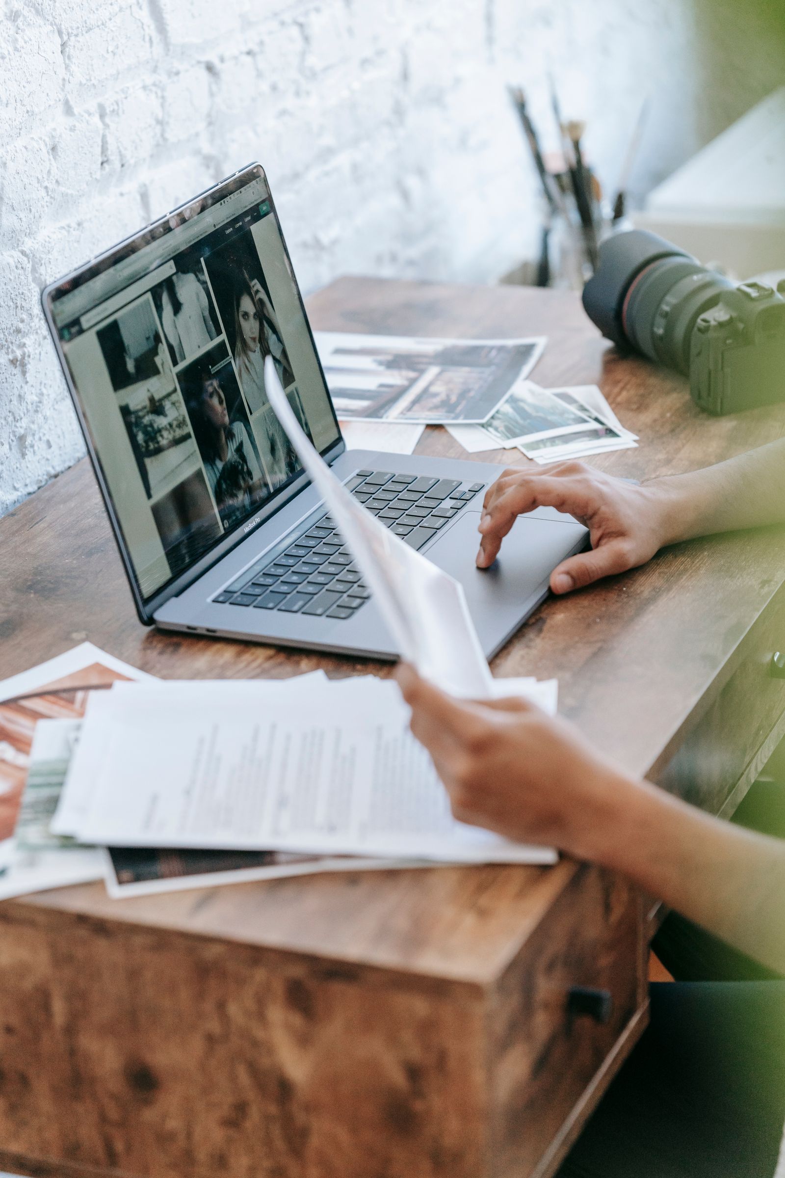 Photographer reviewing printed images and notes beside a laptop
